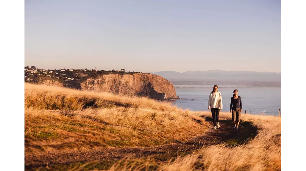 Ladies walking around Taylors Mistake with Christchurch City and the ocean in the background.