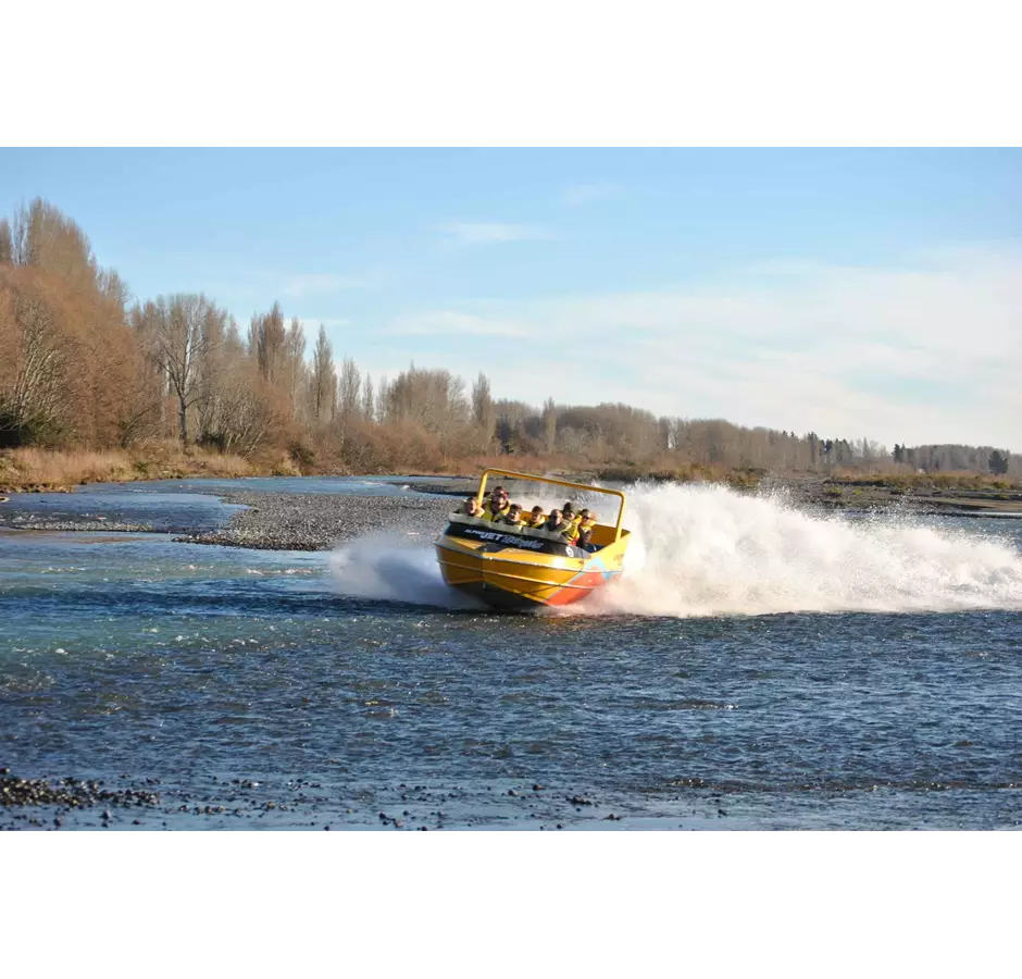 A yellow and orange jet boat heading towards the camera, along the shallow river